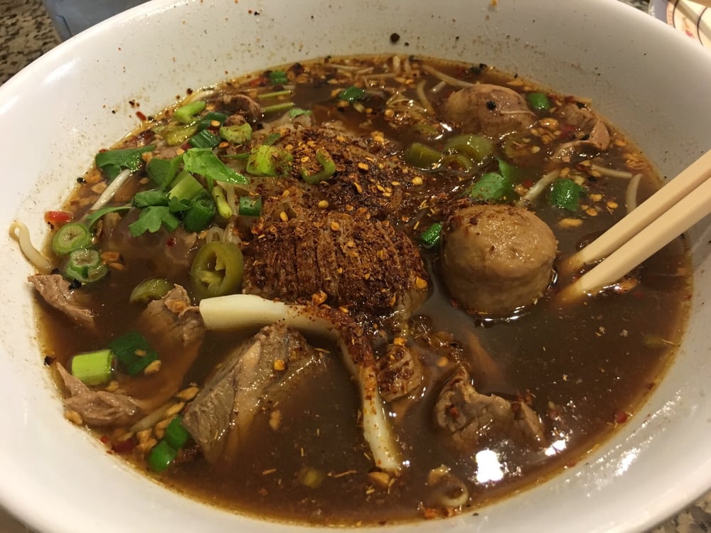 Dark beef noodle soup with meatballs, herbs and chili